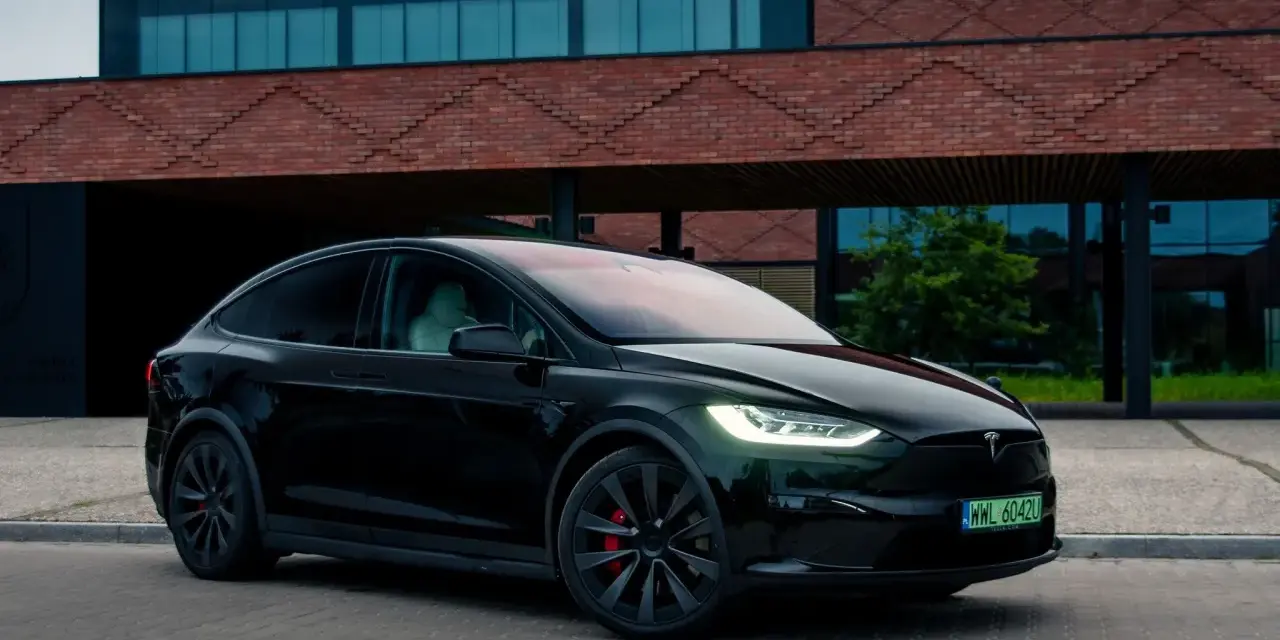 Czarny Tesla Model X zaparkowany przed nowoczesnym budynkiem z cegły.