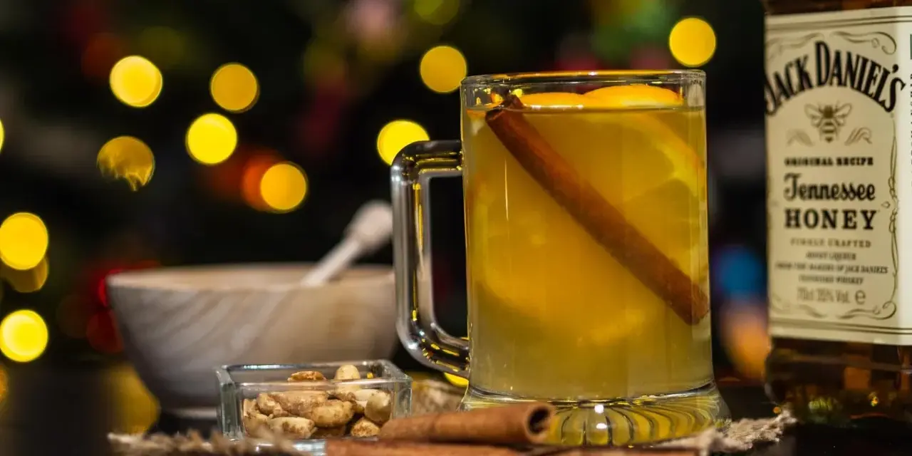 Rozgrzewający drink z Jack Daniels Tennessee Honey, z pomarańczą i cynamonem, w blasku świątecznych światełek.