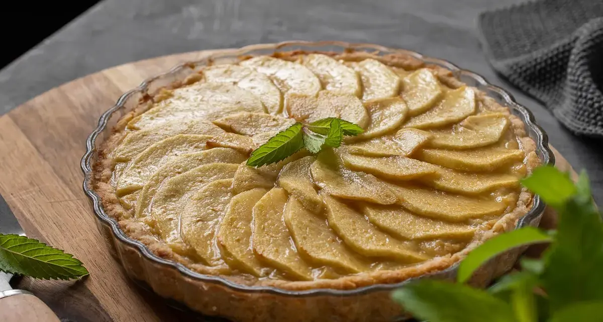 Tarta de manzana casera, con láminas de manzana doradas y una hoja de menta fresca en el centro.