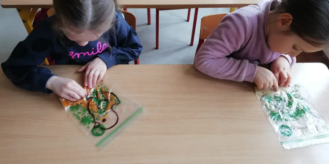 Dwie dziewczynki bawią się materiałami sensorycznymi w woreczkach na drewnianym stole.