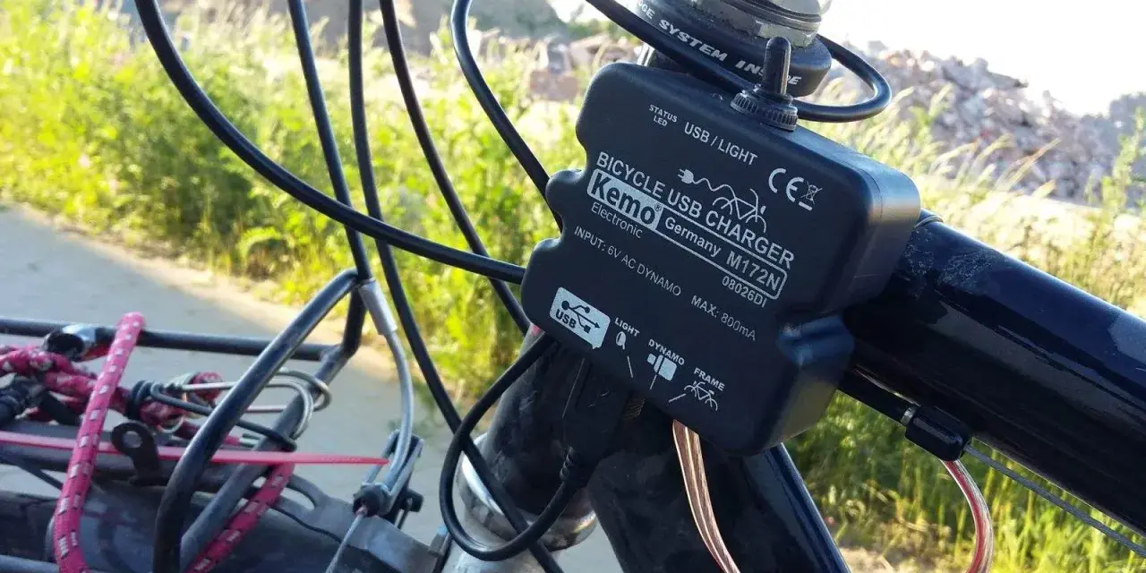 Ładowarka rowerowa Kemo zasilana przez **dynamo**, podłączona do kierownicy, z kablem USB.