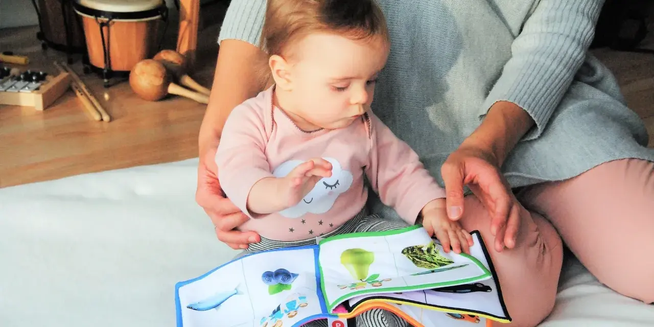 Baby lernt mit einem Stoffbuch und Musikinstrumenten. Förderung der sprachentwicklung baby.