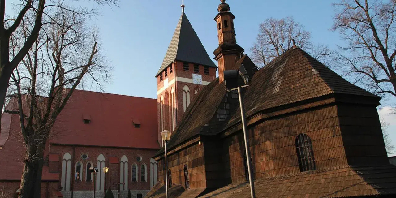 Drewniana i ceglana architektura kościołów w miasteczku śląskim, z wieżą zegarową i strzelistymi dachami, pod błękitnym niebem.
