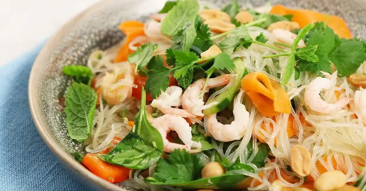 En läcker asiatisk nudelsallad med räkor, morötter, gurka, jordnötter och färska örter.