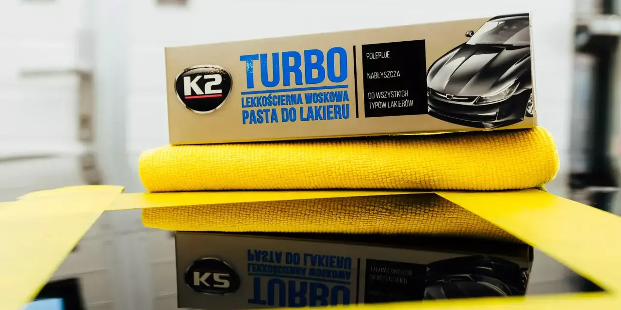 Pudełko pasty do lakieru K2 Turbo i żółta mikrofibra na lustrzanej powierzchni.