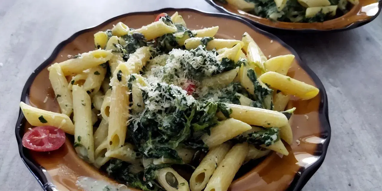 Penne z fetą i szpinakiem, posypane parmezanem. Prosty przepis na makaron ze szpinakiem i fetą.