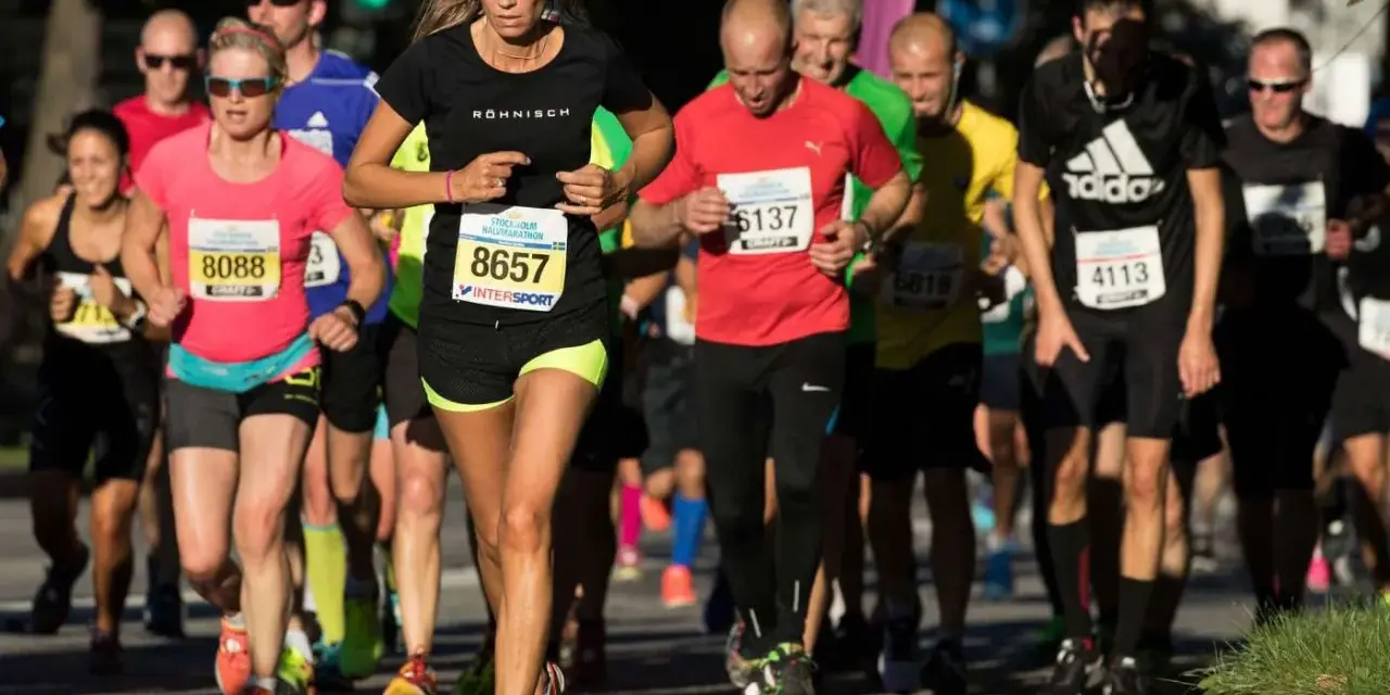 Kvinnlig löpare i täten under Stockholm tempo halvmaraton. Många löpare i olika färger på kläderna.