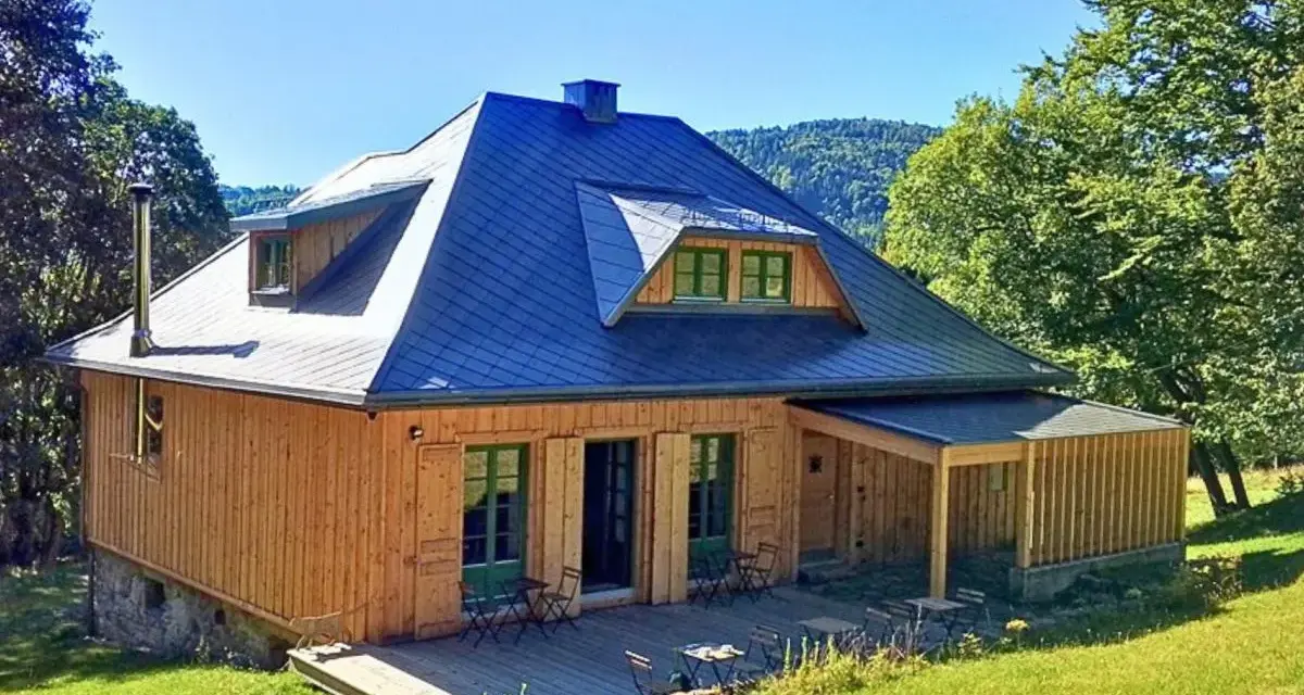 Drewniany domek z niebieskim dachem, tarasem i zielonymi okiennicami. Idealne schronisko oźna na górskim stoku.