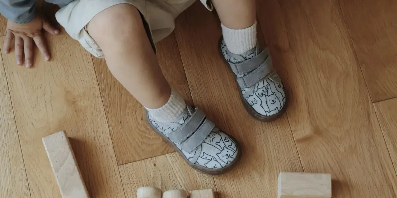 Roczne dziecko bawi się klockami na drewnianej podłodze. Ma na sobie buty z kotkami, idealne do chodzenia po domu.