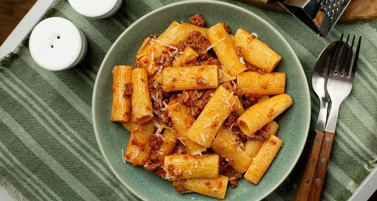 Pyszne makaron grube rurki z sosem bolońskim i parmezanem, gotowe do jedzenia.