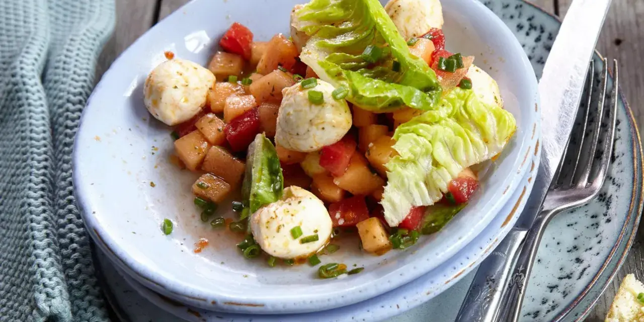 Erfrischender melonensalat mit mozzarella, Tomaten und knackigem Salat. Ein leichter Genuss für warme Tage.