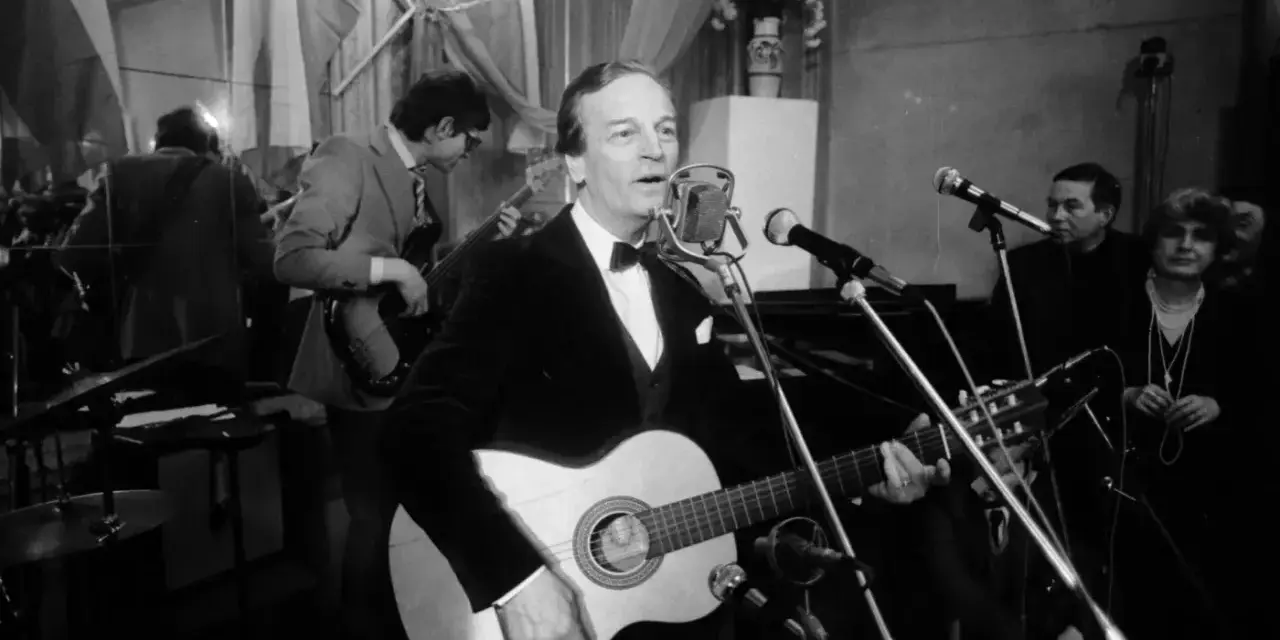 Zbigniew Kurtycz z gitarą i zespołem wykonuje swoje utwory. Wokalista w czarnym aksamitnym fraku śpiewa do mikrofonu.