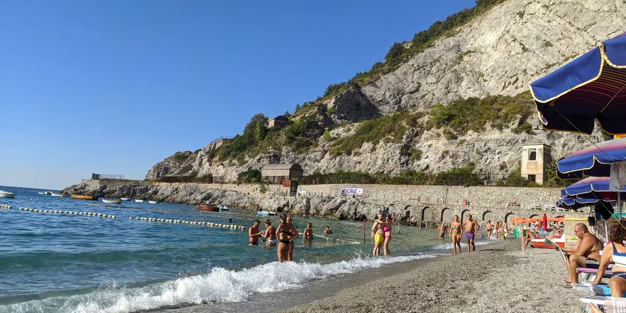 Persone si godono una giornata di sole sulla spiaggia di Erchie, con il mare azzurro e una scogliera imponente alle spalle.