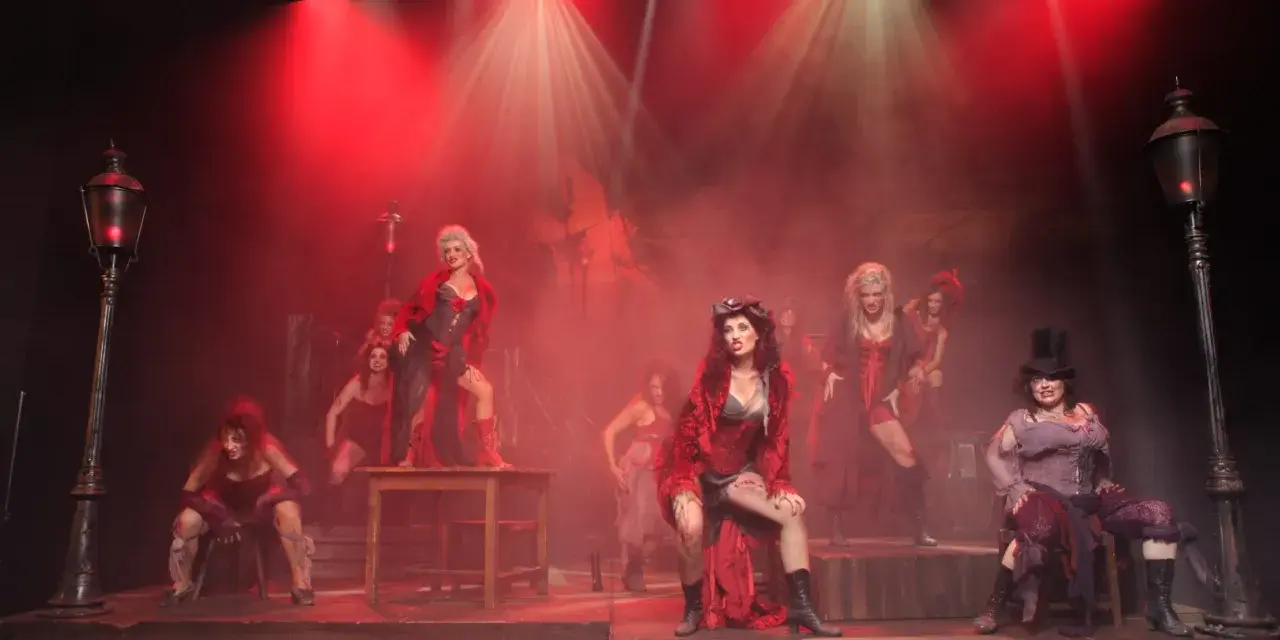 Scena z musicalu "Les Miserables" z kobietami w strojach z epoki, w czerwonym świetle i dymie.