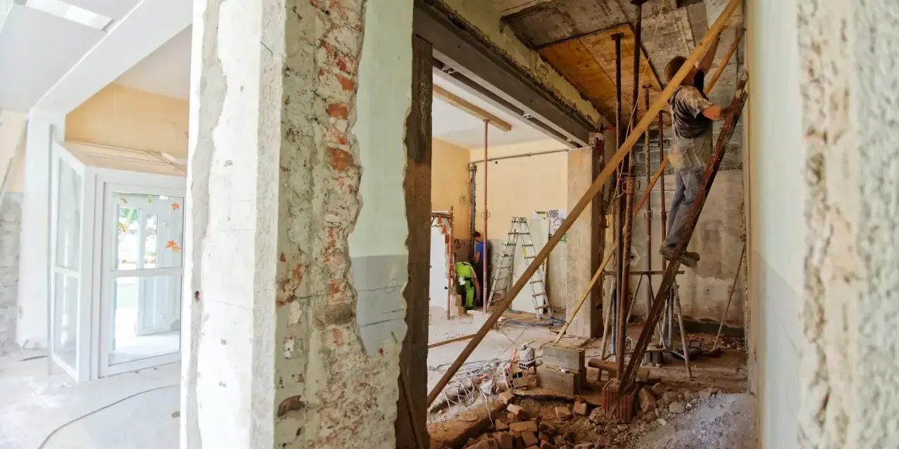 Trwa remont domu. Widać rozbiórkę ścian, gruz i pracowników na drabinach.