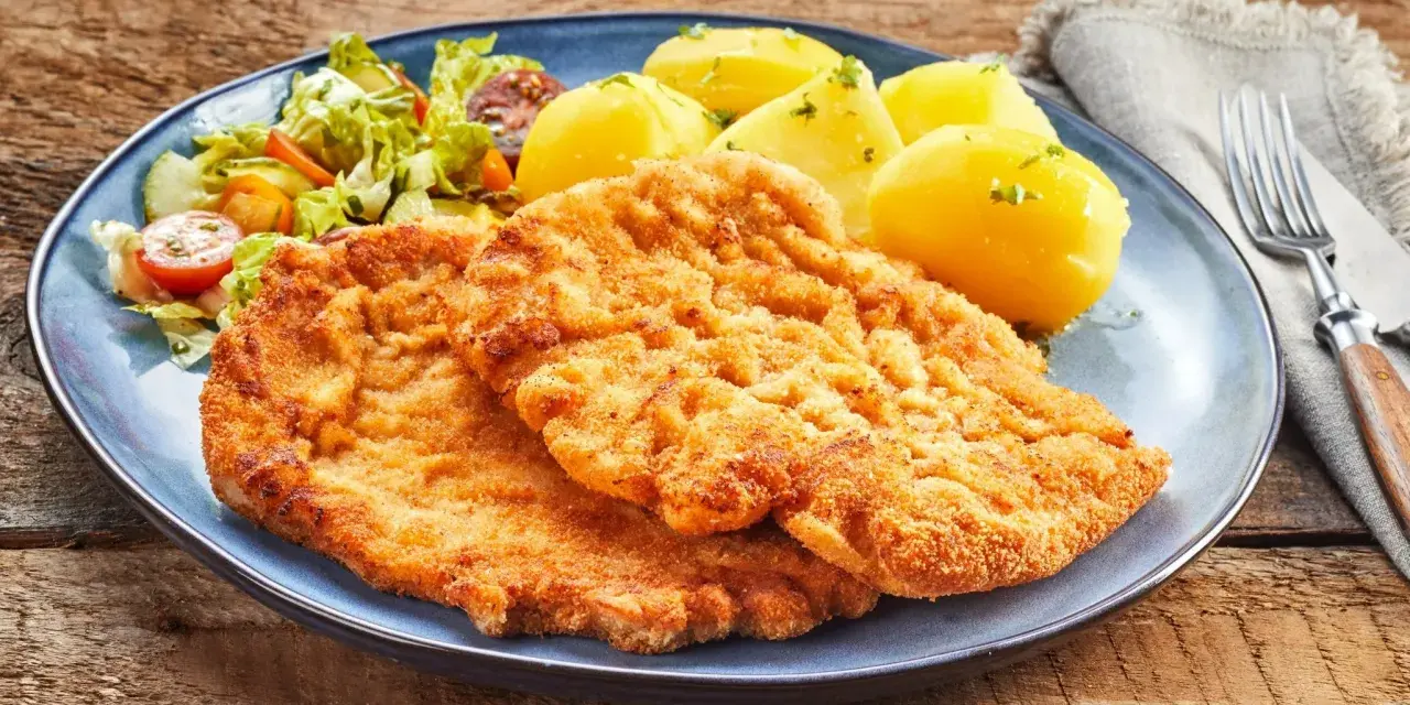 Dwa chrupiące kotlety, jeden sznycel cielęcy, drugi kotlet schabowy, podane z ziemniakami i sałatką.