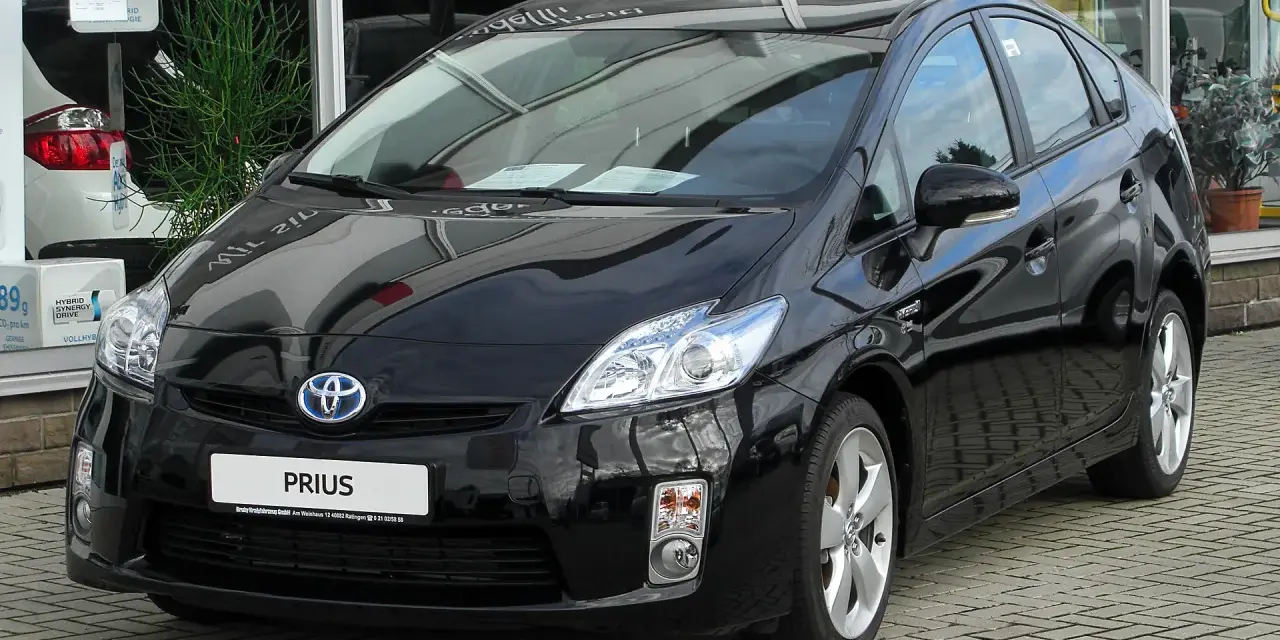 Czarny Toyota Prius 3, hybrydowy samochód, lśni na tle salonu samochodowego.