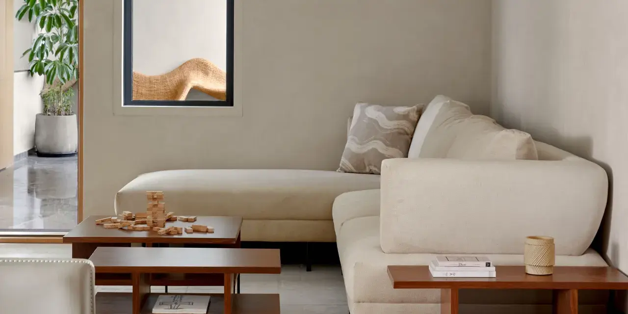 Sofá modular beige, mesa de centro de madera con juego de Jenga, planta en maceta y ventana con detalle decorativo. Ambiente de estilo cozy.