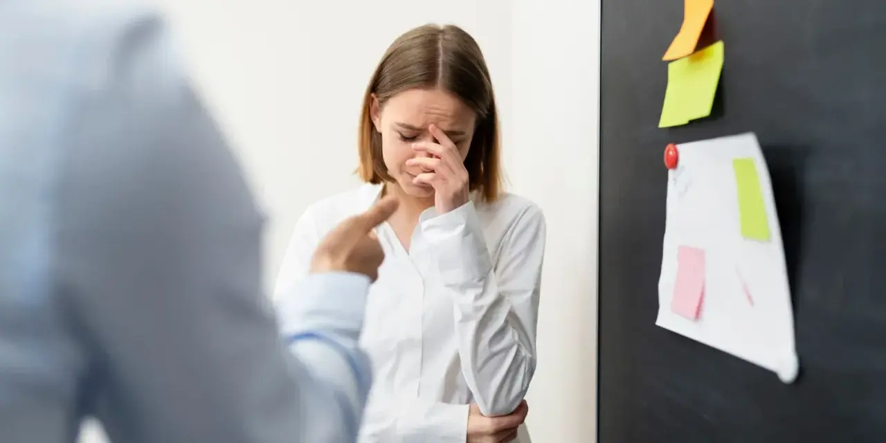 Mujer llora mientras un colega la señala, sufriendo acoso laboral.