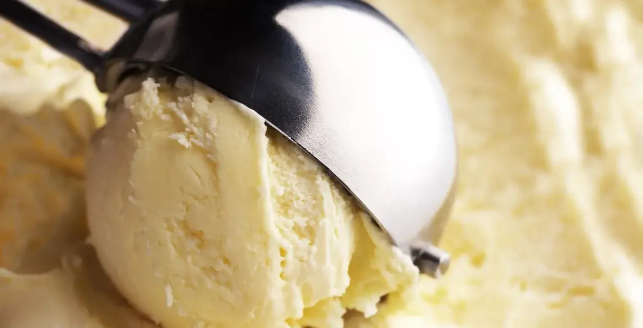 Un cucchiaio raccoglie una pallina di cremoso gelato con yogurt greco, pronto per essere gustato.