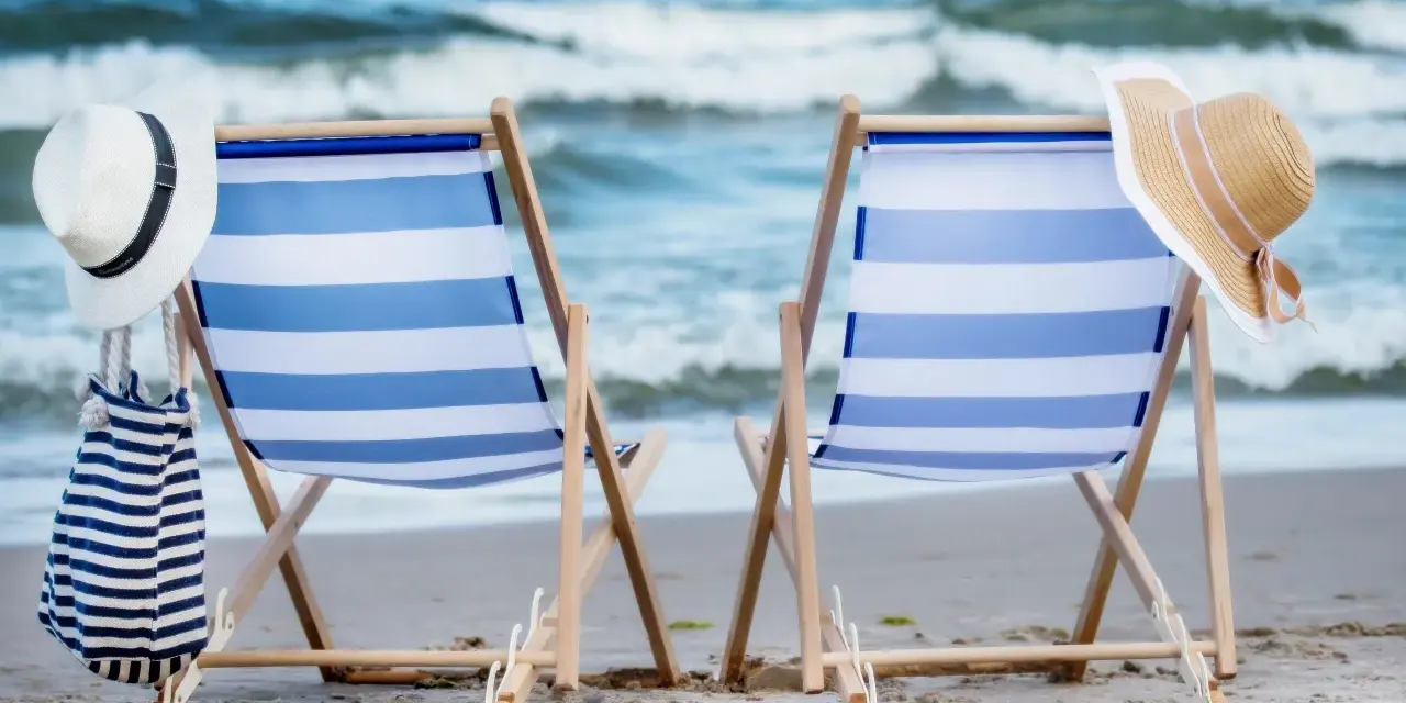 Dwa leżaki z niebiesko-białymi pasami, plażowe kapelusze i torba. Idealne miejsce na sea camp.