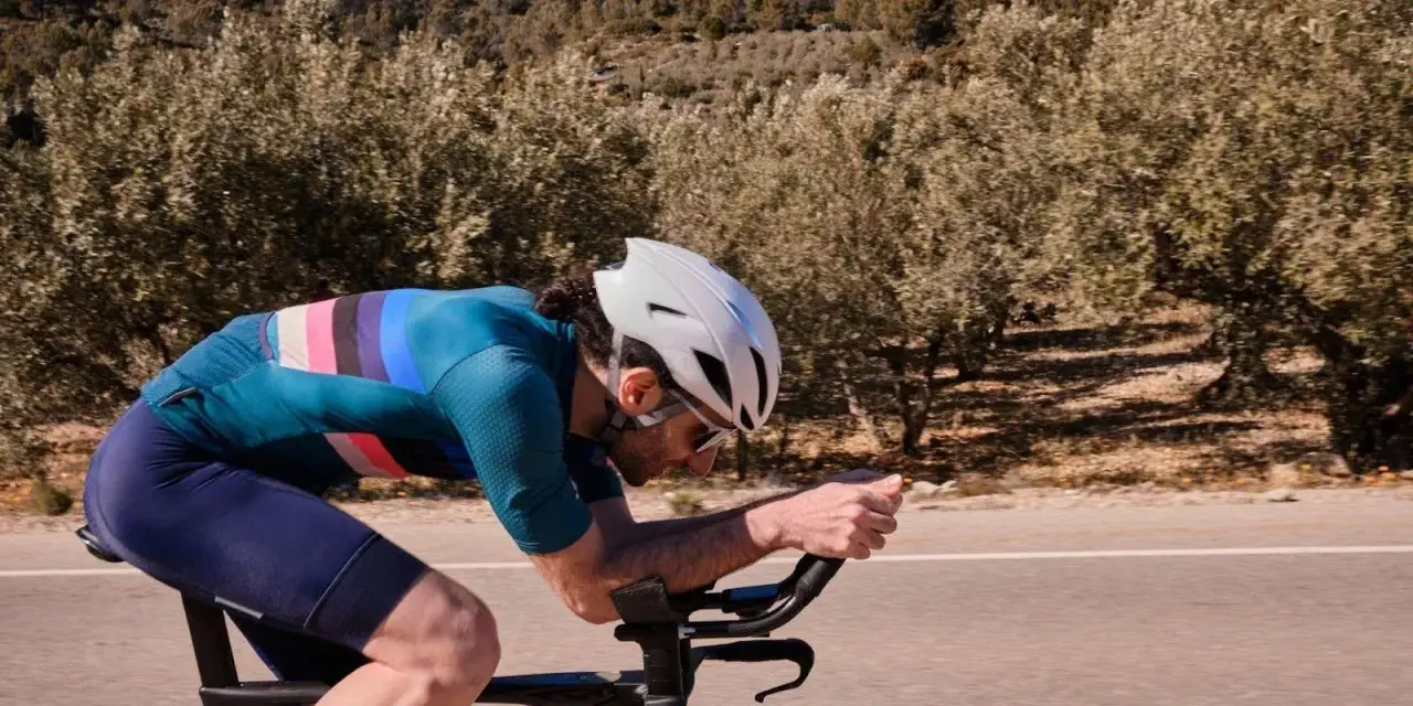 Cyclist pushing hard on a road bike, focused on a VO2 max workout amidst a scenic, tree-lined landscape.