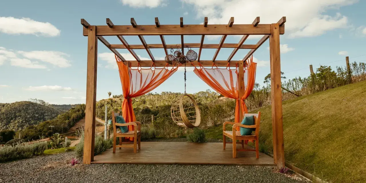 En vacker träpergola med orange draperier och hängstol. Perfekt för att bygga pergola på altan och njuta av utsikten.