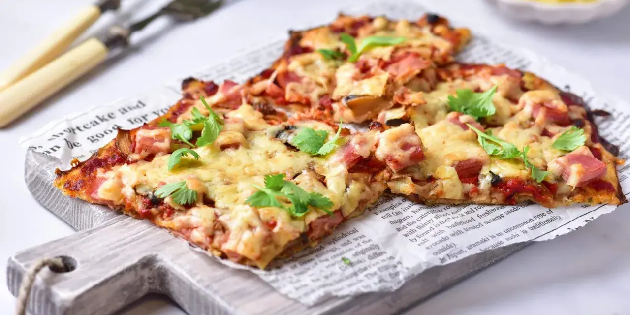 Pyszna pizza na spodzie z kalafiora keto, z szynką i serem, udekorowana świeżą pietruszką.