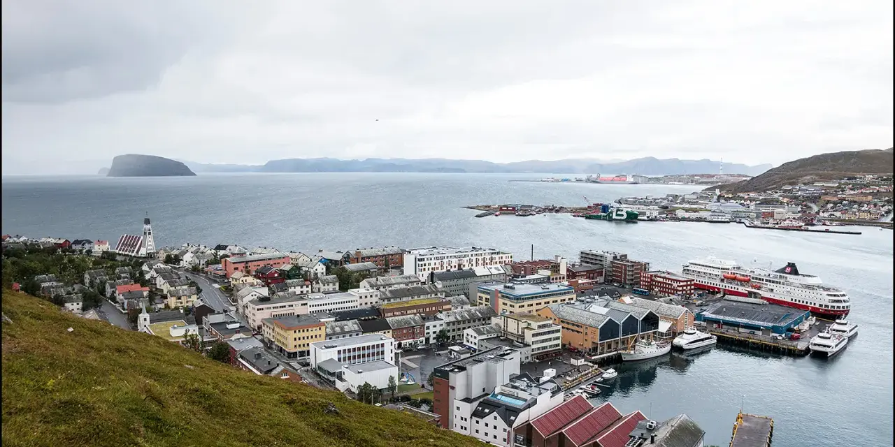 Vy över en stad vid havet med färjor vid kaj. En kyrka med högt torn syns i förgrunden. Detta är Norges nordligaste stad.