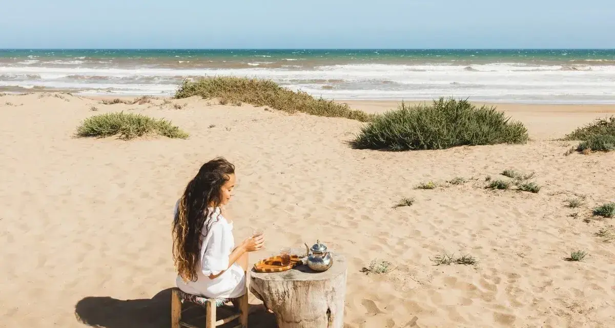 Kobieta pije herbatę na plaży, delektując się widokiem na wzburzone morze. To właśnie takie morze można podziwiać w Tunezji.