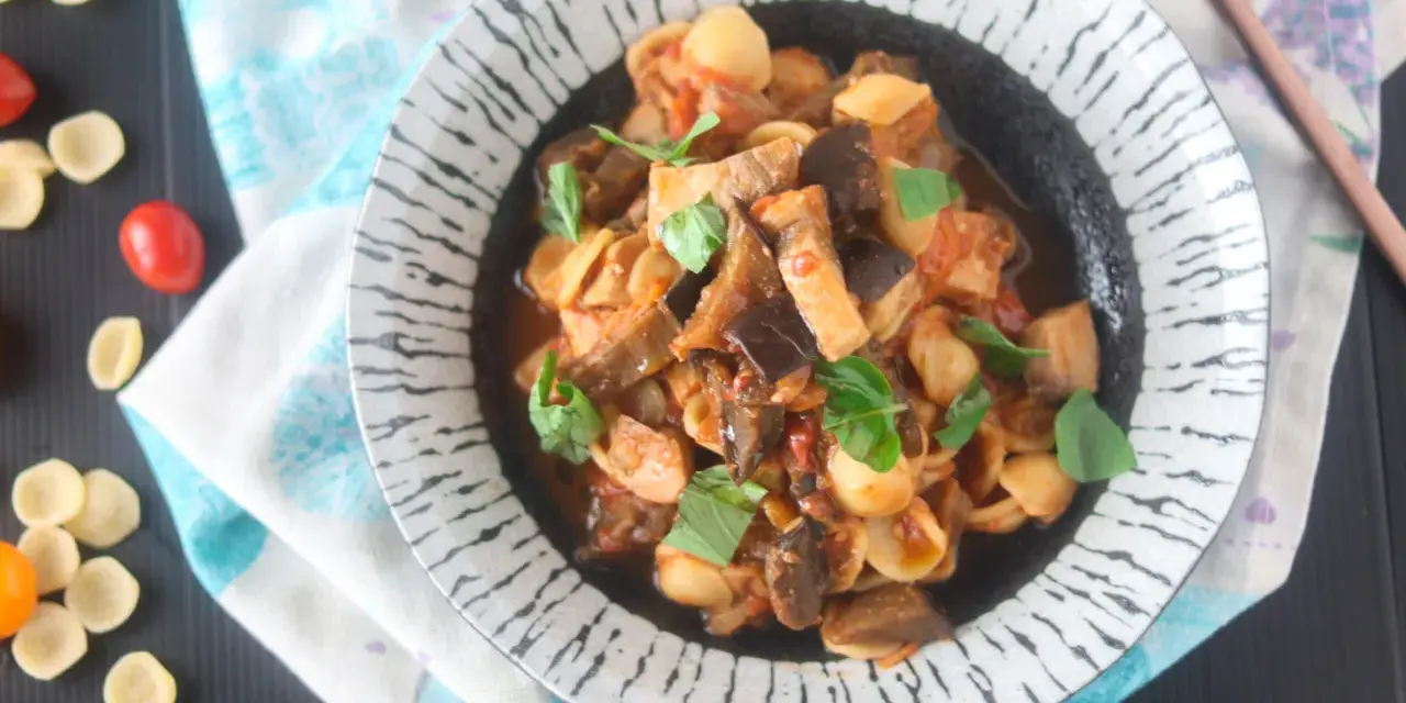Orecchiette con pesce spada e melanzane, un piatto saporito e colorato, guarnito con basilico fresco.