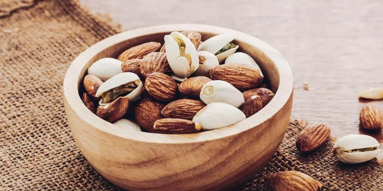 Un bol en bois rempli d'amandes et de pistaches, une liste d'oléagineux parfaite pour une collation saine.