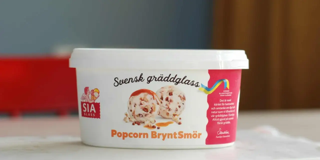 En burk SIA gräddglass med smak av popcorn och brynt smör. Glasskulor med kolasås och popcorn syns på etiketten.