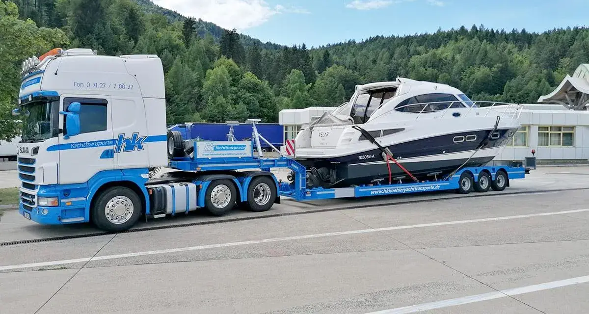 Ein LKW transportiert ein luxuriöses Boot auf einem Spezialanhänger. Die Yacht ist sicher auf dem Anhänger befestigt, bereit für den Transport über Land.