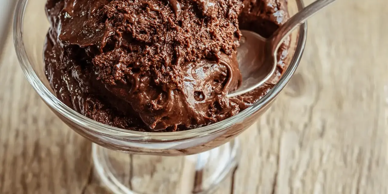 Une cuillère s'enfonce dans une coupe de mousse au chocolat au lait onctueuse, prête à être dégustée.