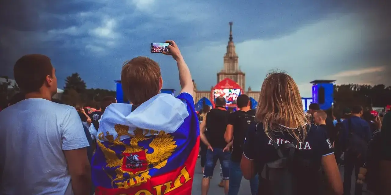 Fani w moskiewskim klubie piłkarskim, jeden z nich z flagą Rosji, nagrywa telefonem koncert.
