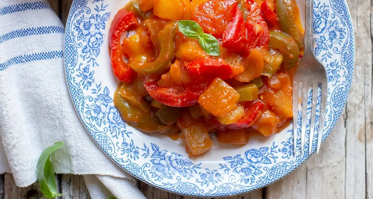 Un piatto di peperonata con patate, colorata e saporita, guarnita con basilico fresco.