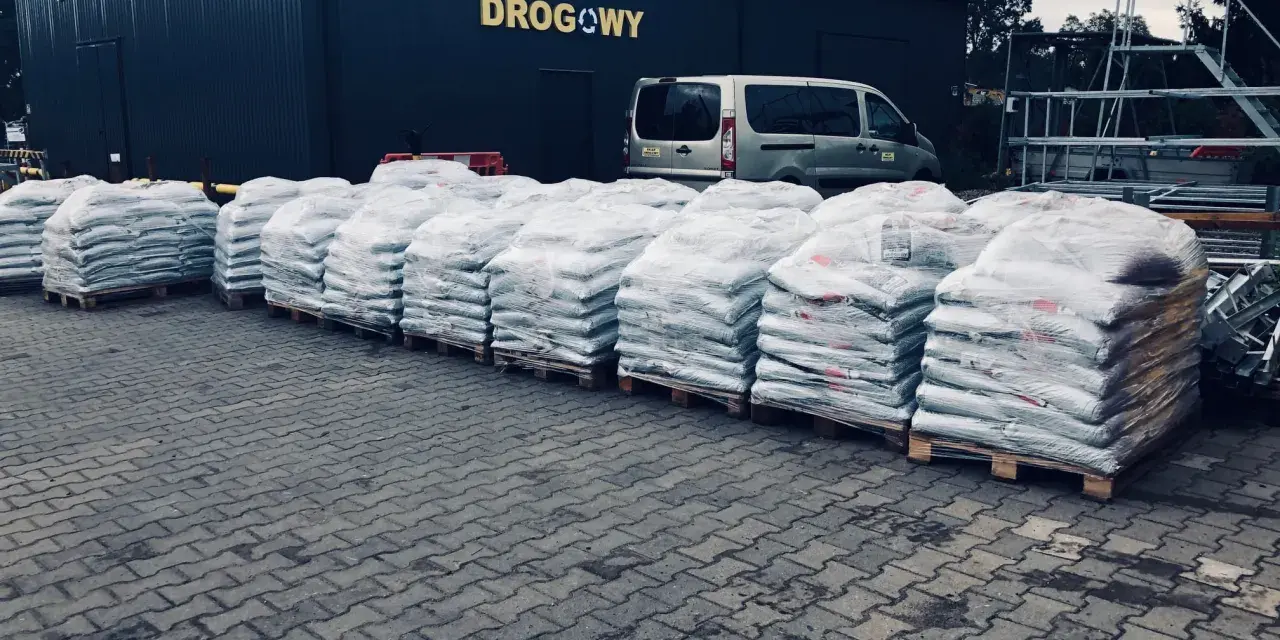 Duże worki z materiałem budowlanym przed sklepem drogowym. Zastanawiasz się, ile kosztuje asfalt? Tutaj znajdziesz odpowiedź.