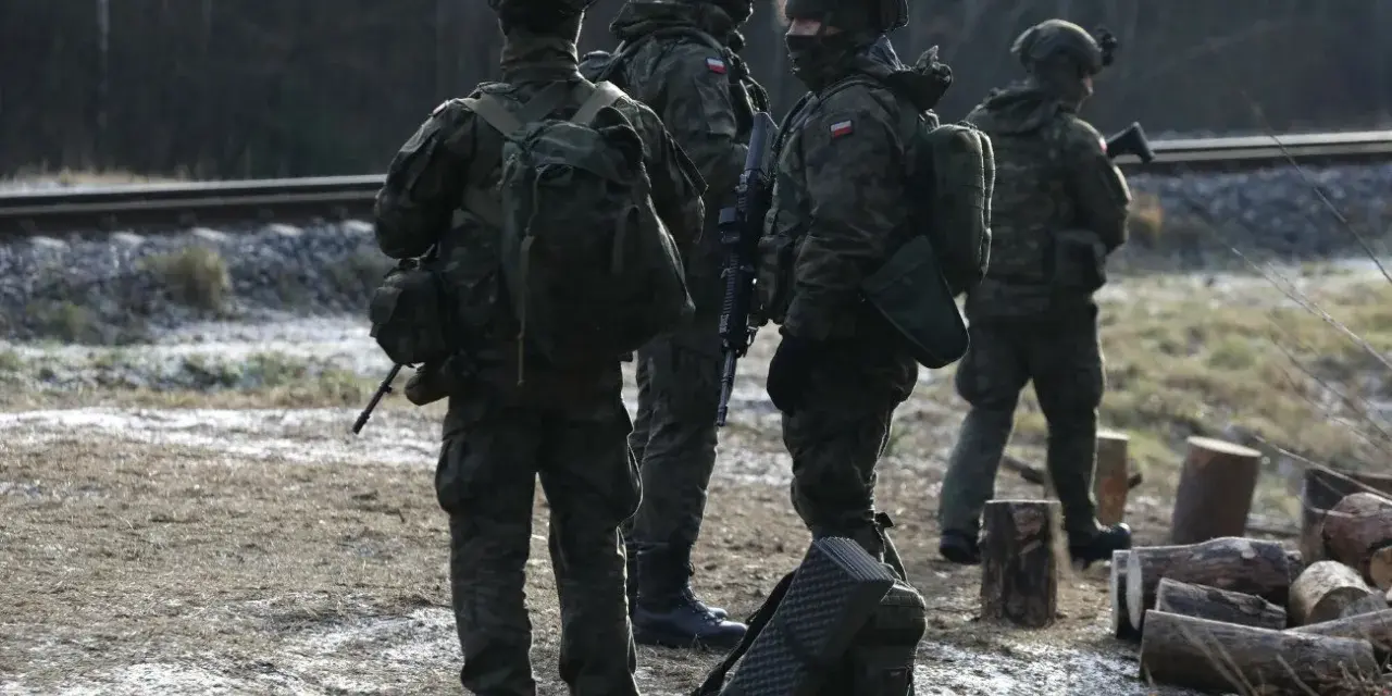 Szeregowi w wojsku patrolują teren przy torach kolejowych, gotowi do akcji.