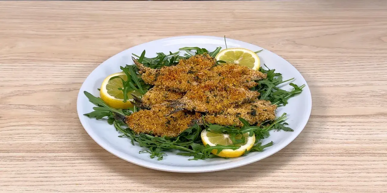 Piatto di alici al forno dorate e croccanti, servite su un letto di rucola fresca con spicchi di limone.