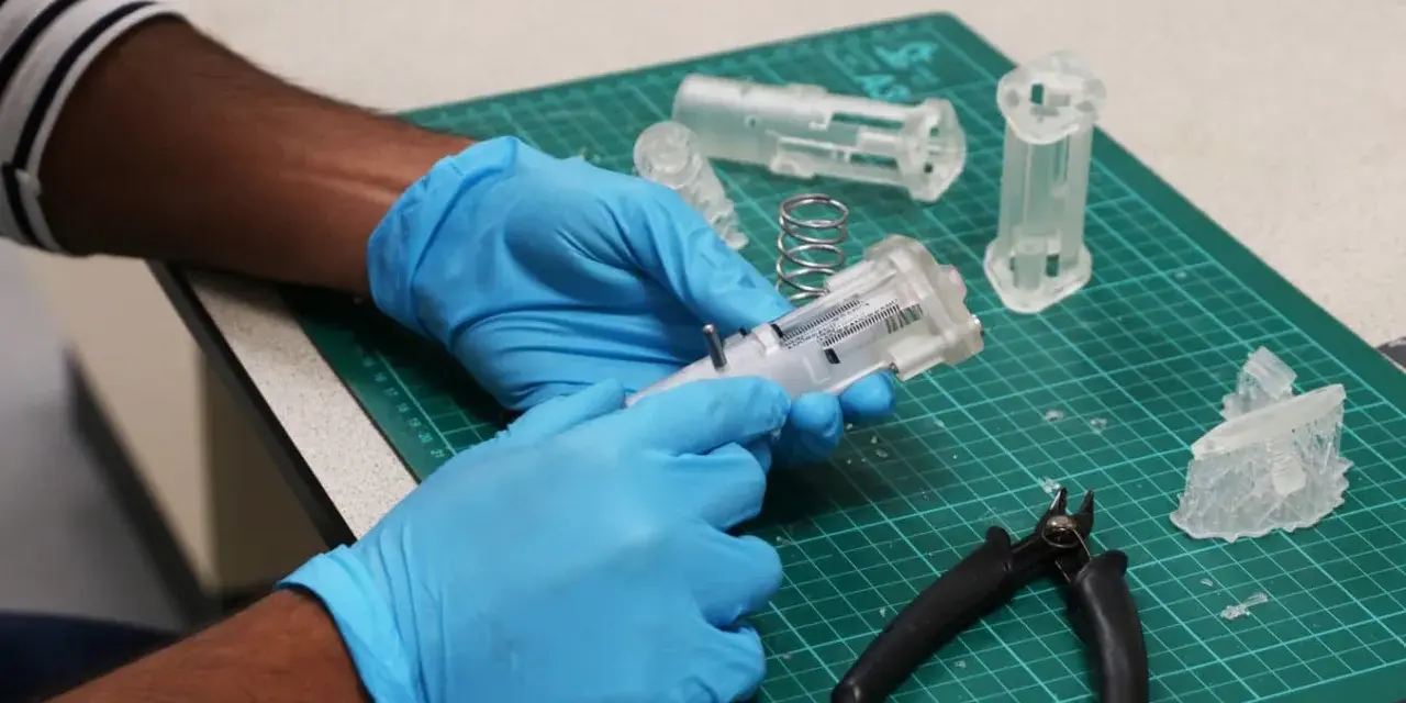 Hands in blue gloves assemble a 3D printed medical device prototype, showcasing innovation in healthcare technology.
