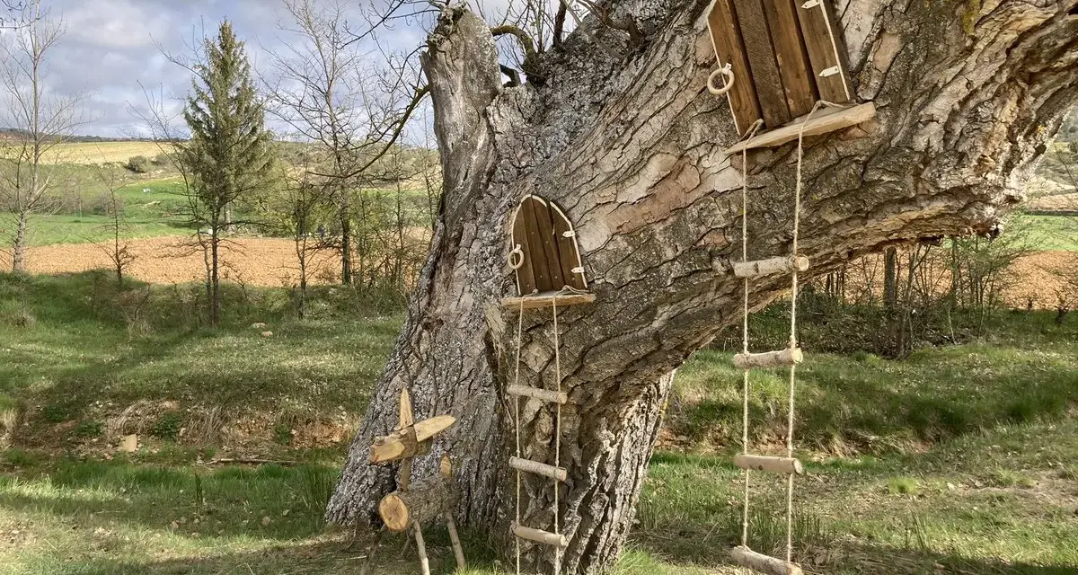 Un árbol con dos pequeñas puertas de madera y escaleras de cuerda, invitando a un arbolón paseo mágico. Un ciervo de madera decora la base.