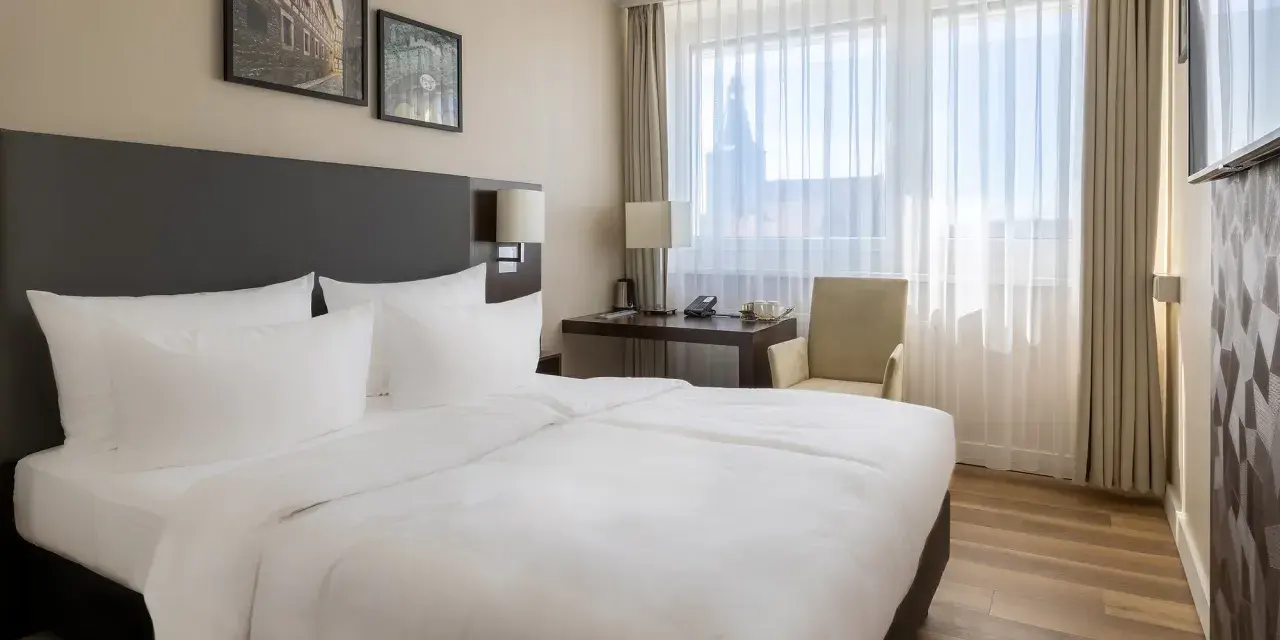 Przytulny pokój w hotelu Radisson Blu Erfurt z białym pościelonym łóżkiem, biurkiem i oknem z widokiem na miasto.