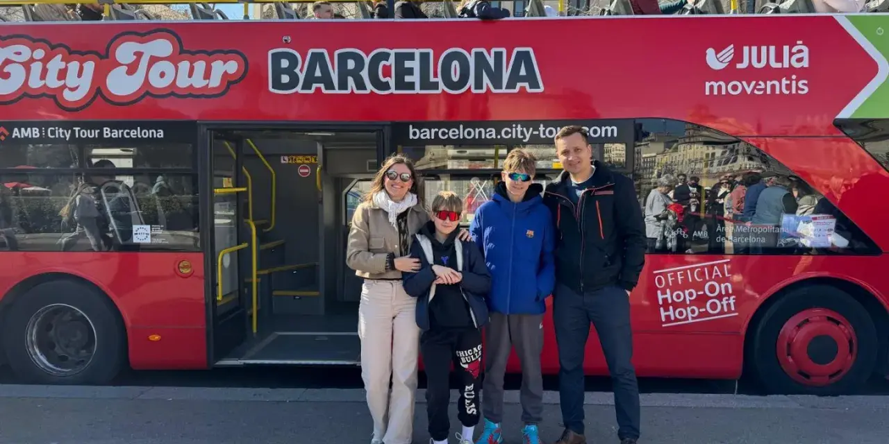 Family posing in front of a red "City Tour Barcelona" bus, ready for an adventure.