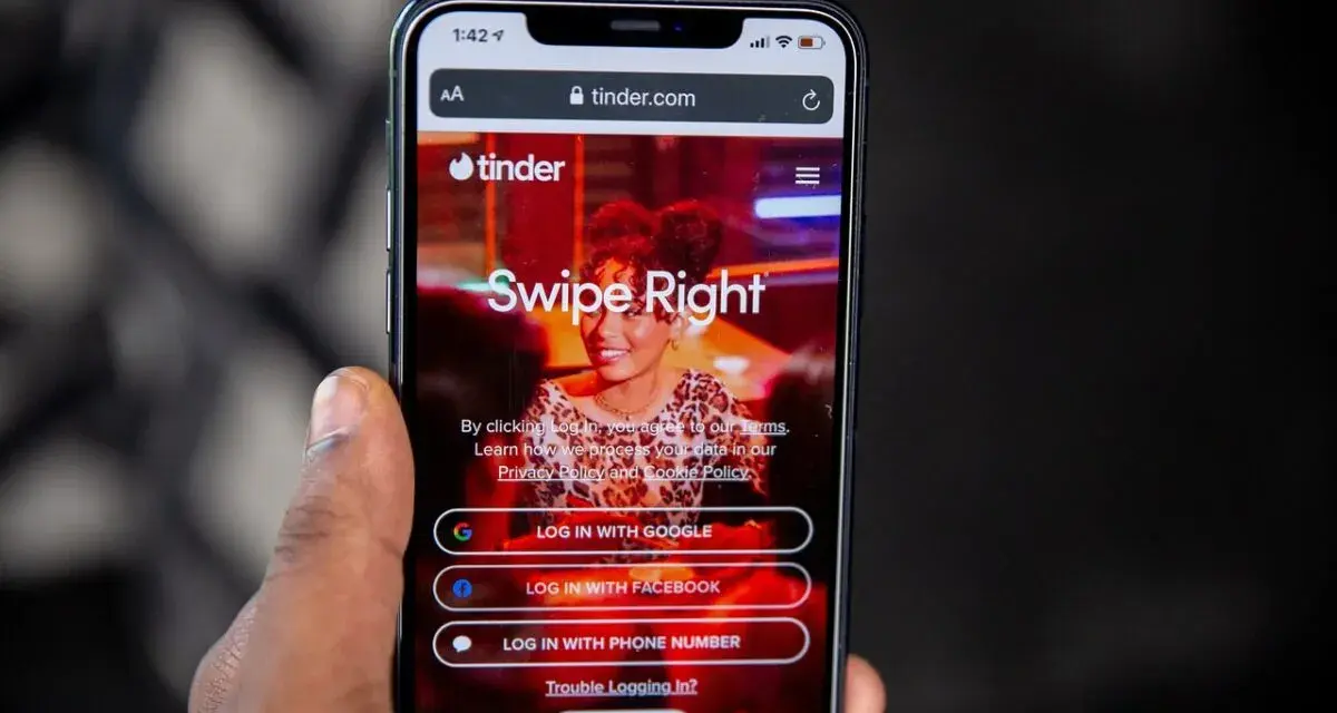 Dłoń trzyma smartfon z otwartą stroną logowania portalu randkowego Tinder. "Swipe Right" zachęca do rozpoczęcia poszukiwań.