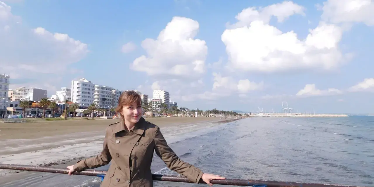 Kobieta na molo, ciesząca się łagodną pogodą w styczniu na Cyprze. W tle plaża i nadmorskie miasto.