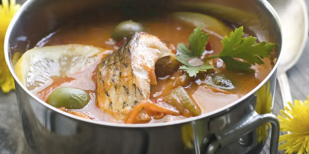 Aromaticzna rosyjska zupa rybna w metalowej misce, z kawałkami ryby, oliwkami, cytryną i natką pietruszki.