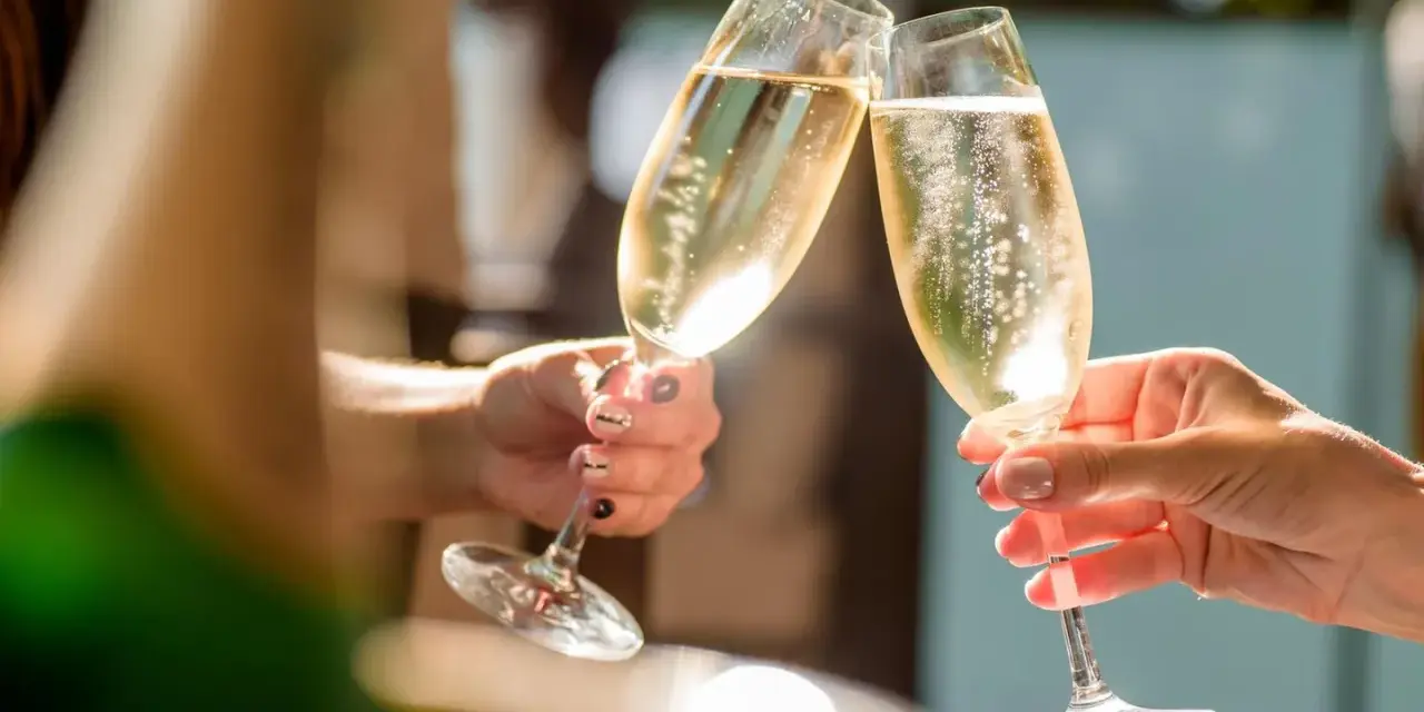 Zwei Hände stoßen mit Gläsern an, gefüllt mit prickelndem alkoholfreiem Sekt. Perfekt für die Schwangerschaft und besondere Anlässe.