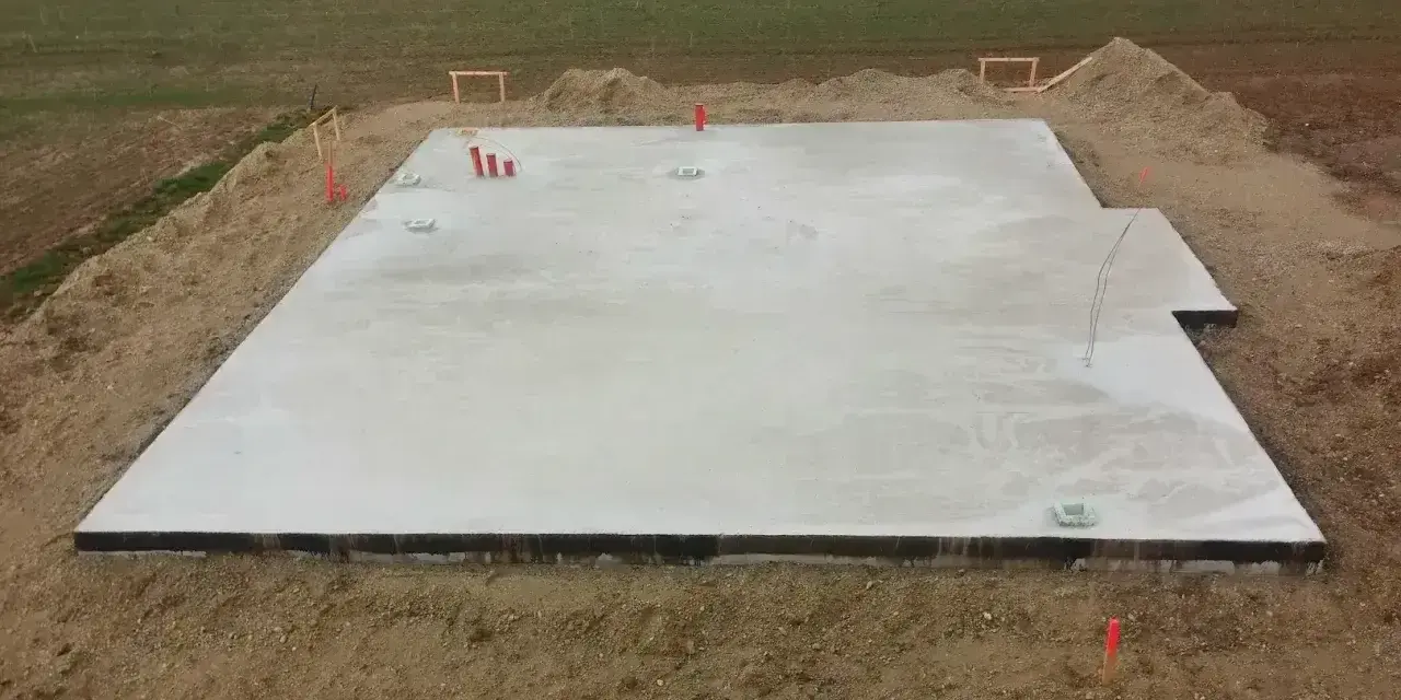 Płyta fundamentowa koszt. Betonowa płyta na budowie, otoczona ziemią i elementami instalacji.