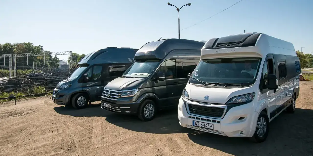 Trzy kampery stoją obok siebie na placu. Jeden z nich to kamper VW w ciemnoszarym kolorze.